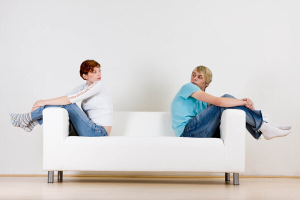 Two friends sitting on opposite ends of a white couch.